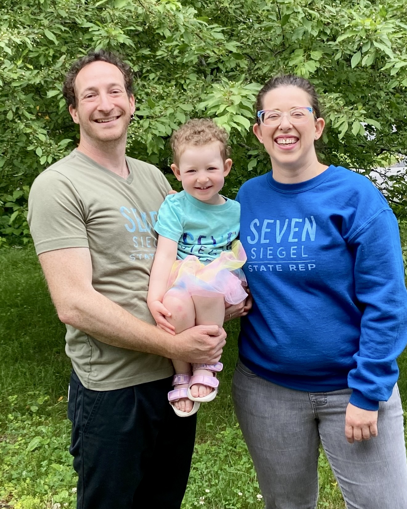 Seven Siegel with their wife Becky Wartell and their young daughter, all smiling outdoors in Seven Siegel campaign shirts