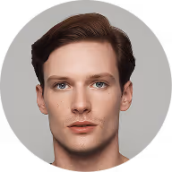Portrait of a young man with short brown hair and blue eyes against a gray background.
