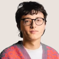 Young person with short dark hair and glasses wearing a red and purple patterned sweater.