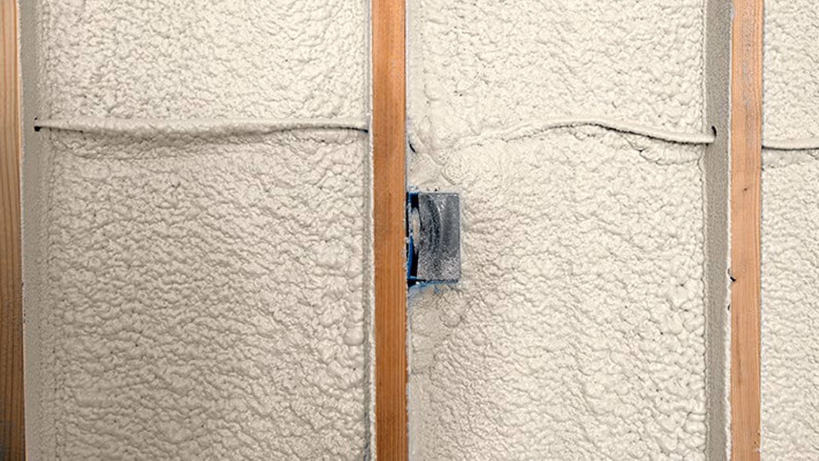 Spray foam insulation applied between wooden studs in a wall with an electrical box embedded.