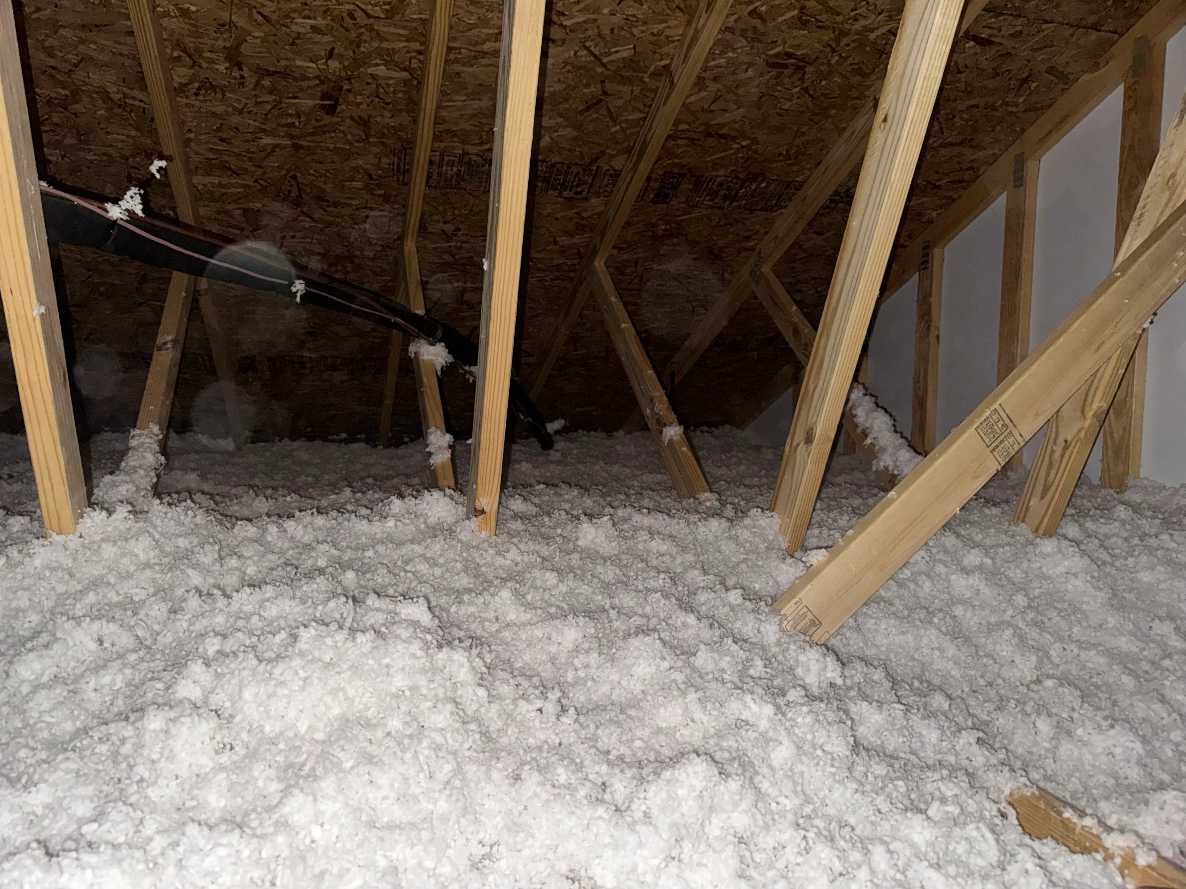 Attic with wooden beams and white loose-fill insulation covering the floor between the joists.