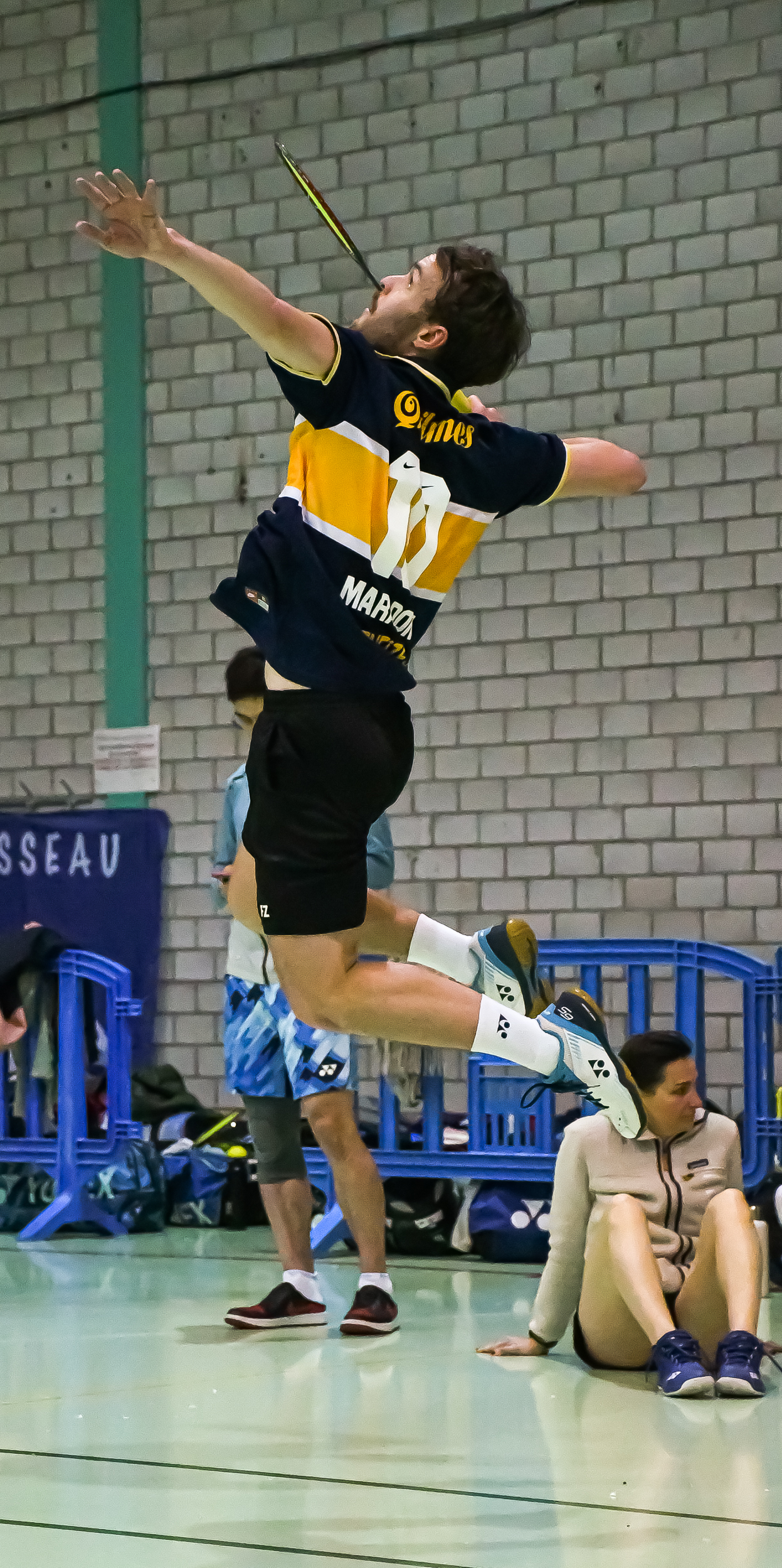 Badminton player in mid-air preparing to hit the shuttlecock during an indoor match.