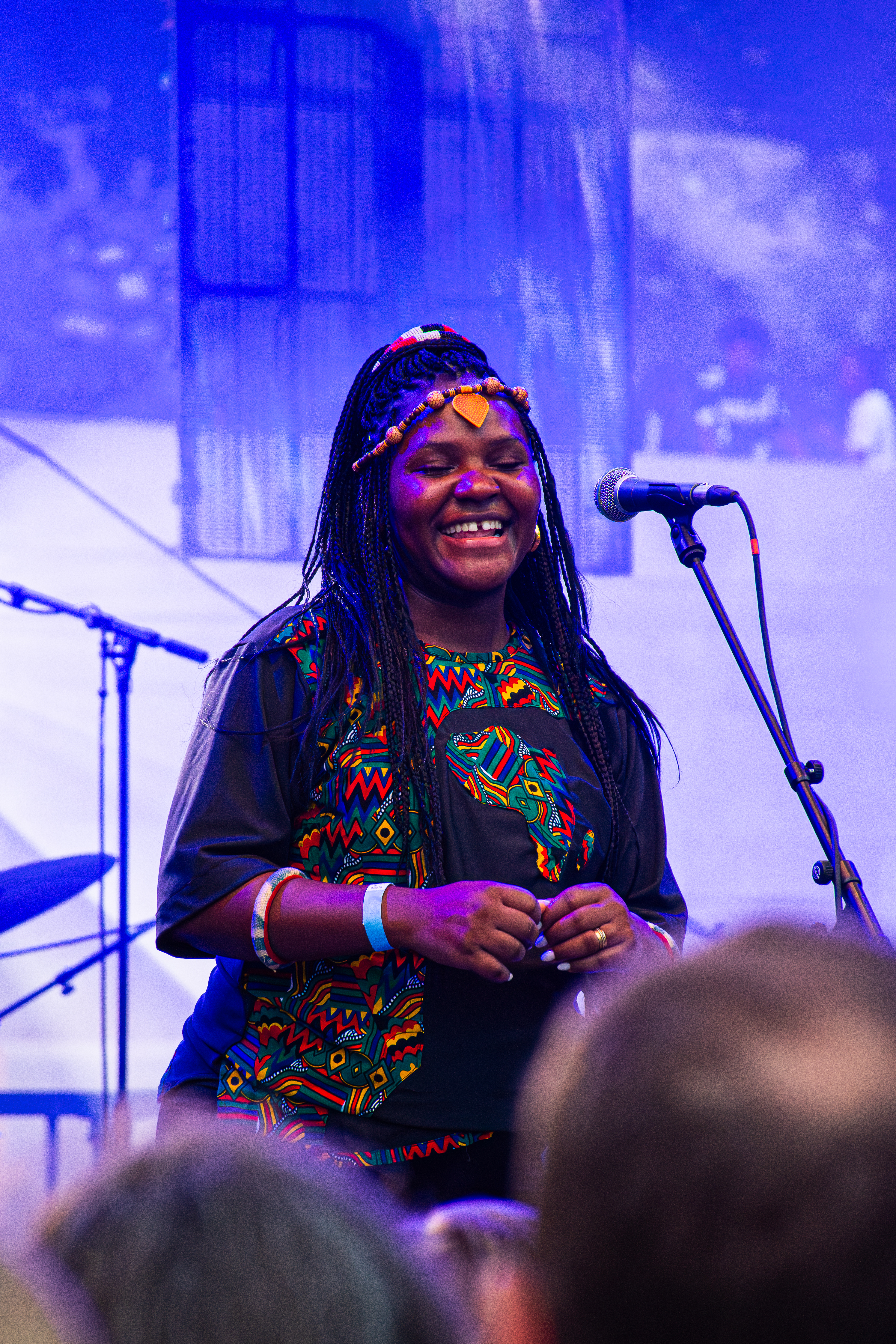Singer performing on stage laughing under blue lighting at music festival