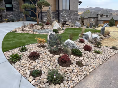 Front yard landscape with artificial green turf, decorative rocks, shrubs, and a small tree near a modern house.