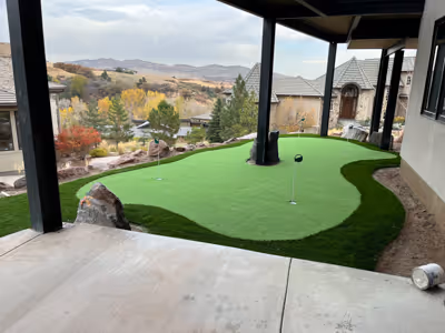 Backyard putting green with two golf holes under a covered patio overlooking a hilly landscape with autumn trees.