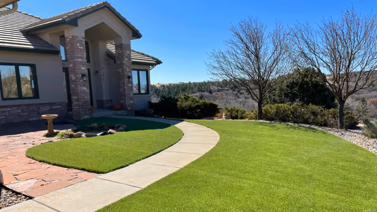 Modern house with a stone and brick facade, a curved concrete walkway, and a well-maintained green lawn with leafless trees in the background under a clear blue sky.