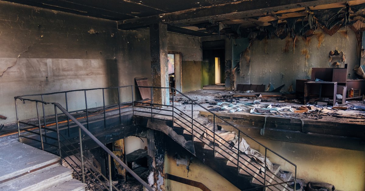 Burned interior of a commercial building. The walls and ceiling are coated with soot, and the floors are covered in debris.