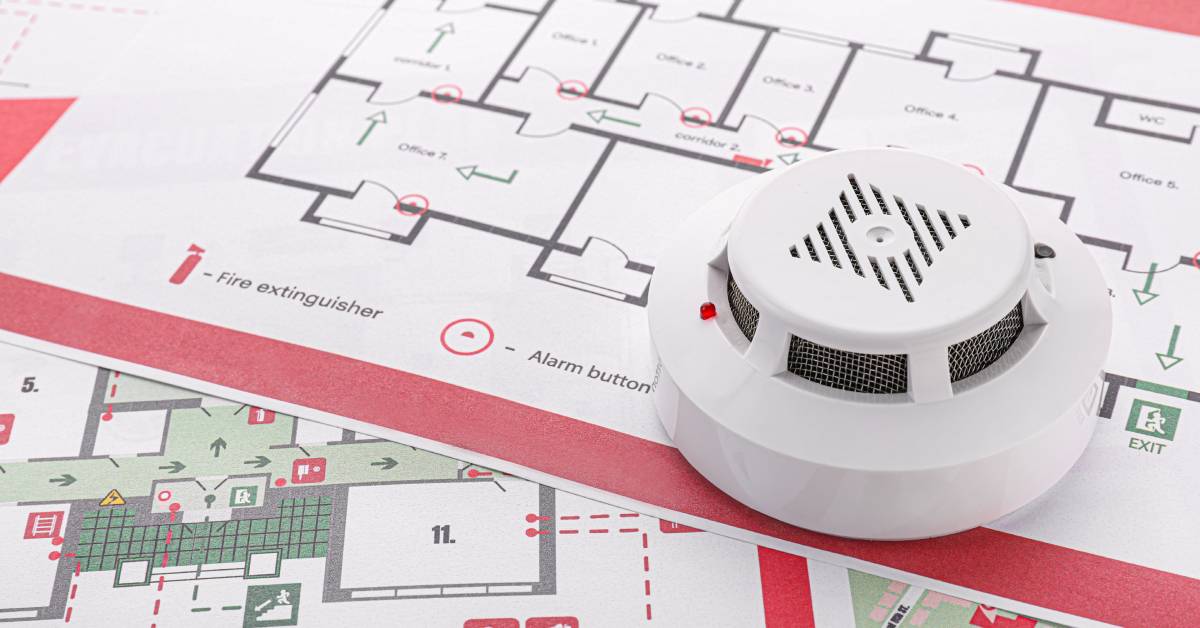 Several sheets of paper containing floor plans showing evacuation routes. A smoke detector is on top of the papers.
