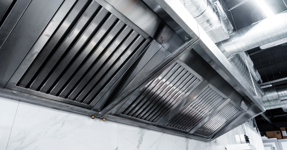 Close-up of stainless steel hoods in a restaurant kitchen. The walls of the kitchen consist of white marble.