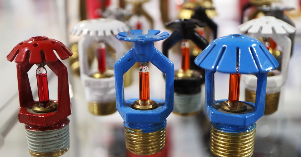 Blue, white, black, red, and unpainted fire sprinkler heads sitting on a table. Their deflectors come in various shapes.