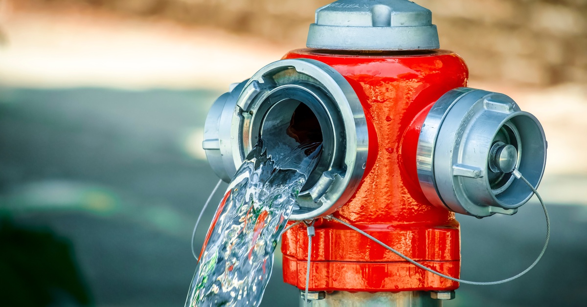 A silver-and-red fire hydrant is missing one of its caps. A stream of clear water pours out of the hole.