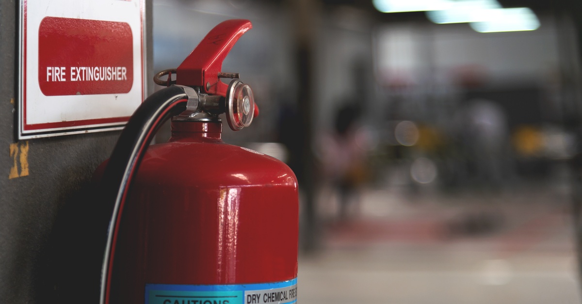 An extinguisher with a caution label sits against a wall with a sign that reads Fire Extinguisher above it.