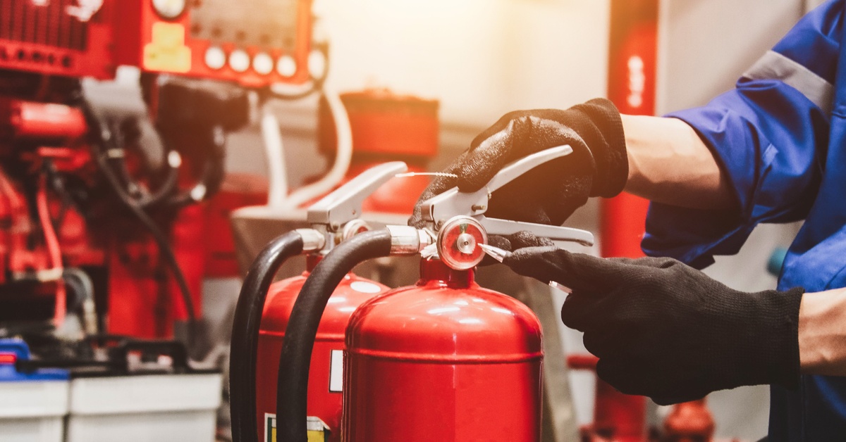 Close-up of red fire extinguishers during an inspection. A person examines them while wearing black gloves.