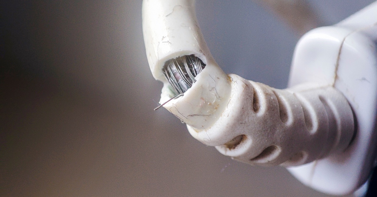 The exterior of an electrical power cord breaks, revealing the circuits underneath. The cable's outside is white.