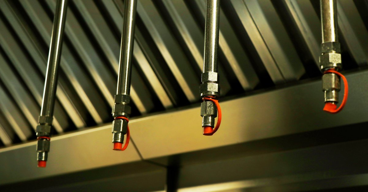 Four fire sprinklers hang from the ceiling in a kitchen with rubber tips on the ends. A ventilation system is behind them.