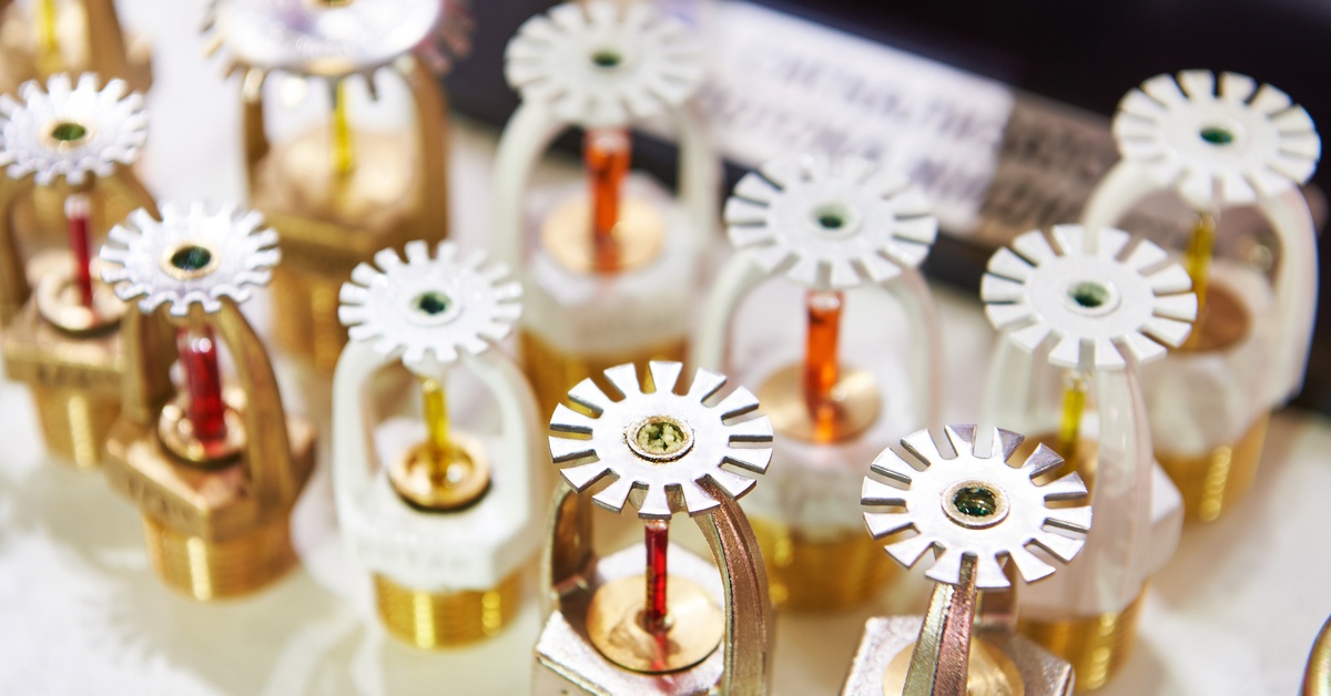 Several fire extinguisher heads sit next to each other on a flat surface. They feature silver, gold, and white components.