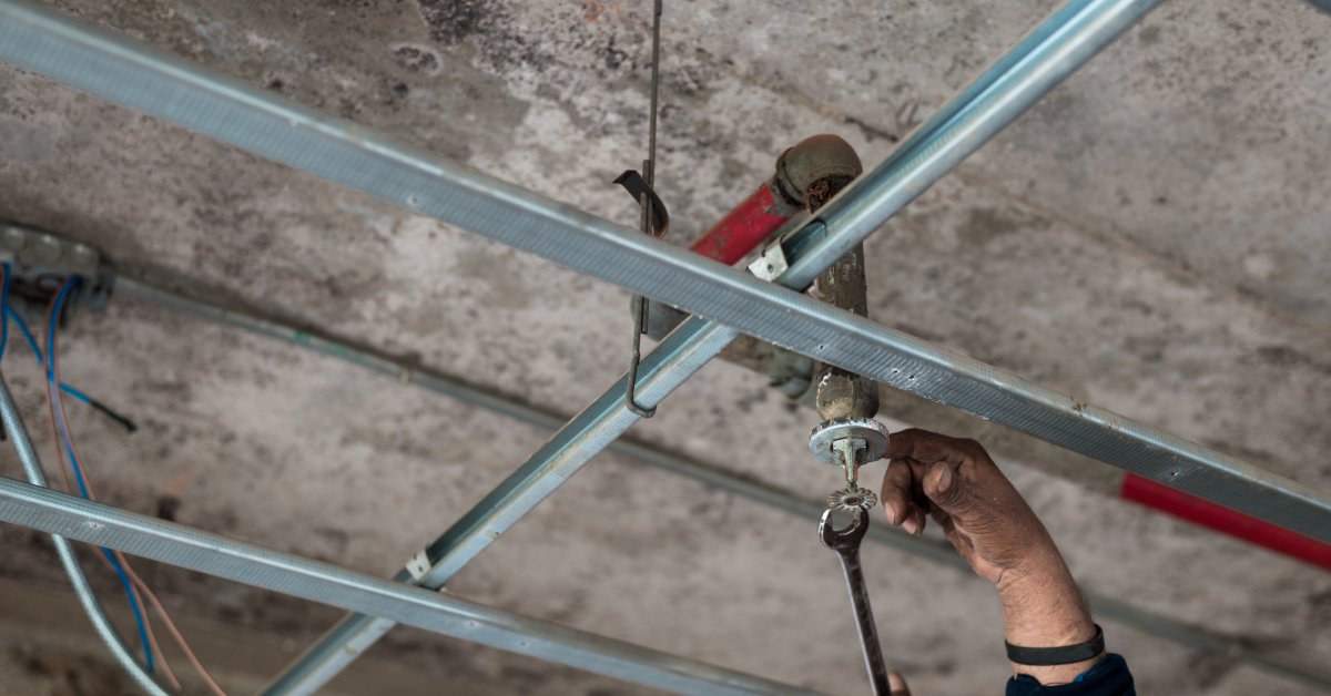 A pair of hands using a wrench to provide maintenance to a sprinkler system . A concrete ceiling is visible in the background.