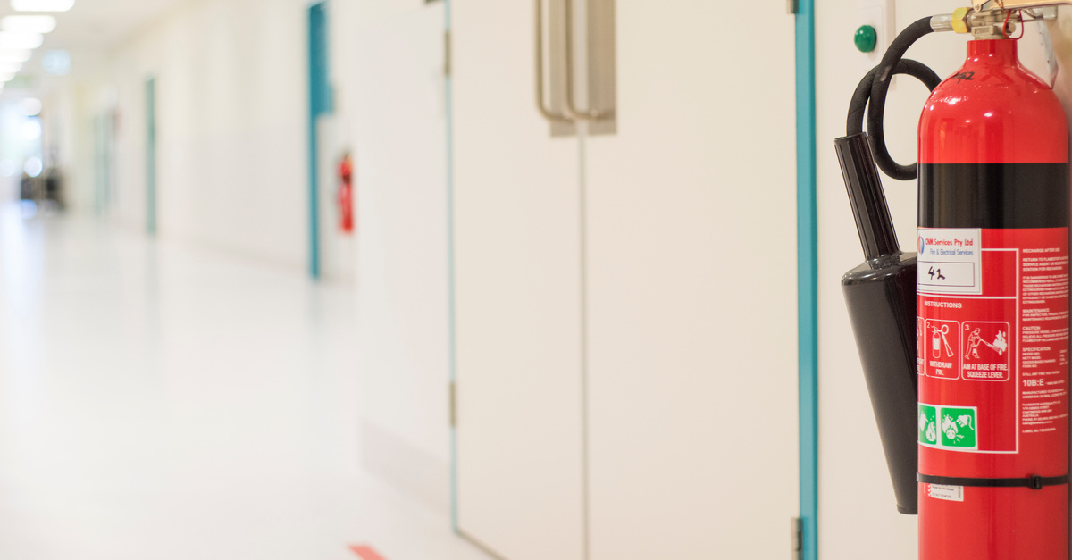 A fire extinguisher mounted on a wall in a long white hallway. It's next to a pair of blue commercial swinging doors.