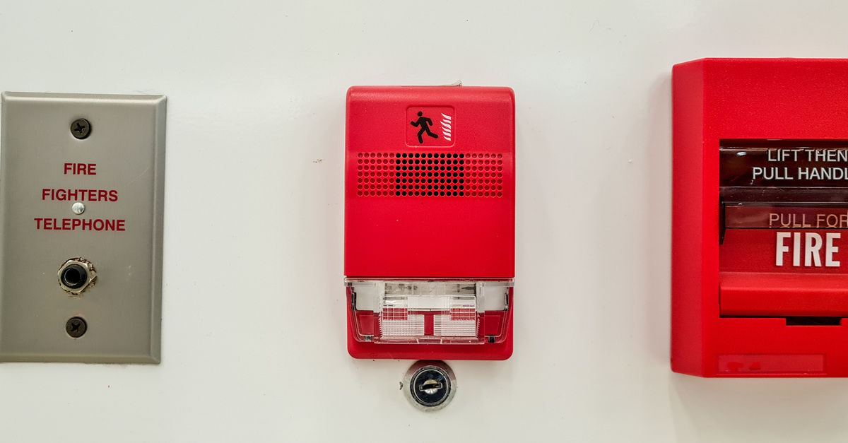 A fire alarm phone jack, a sound and light fire alarm, and a red pull station set up side-by-side on a wall.