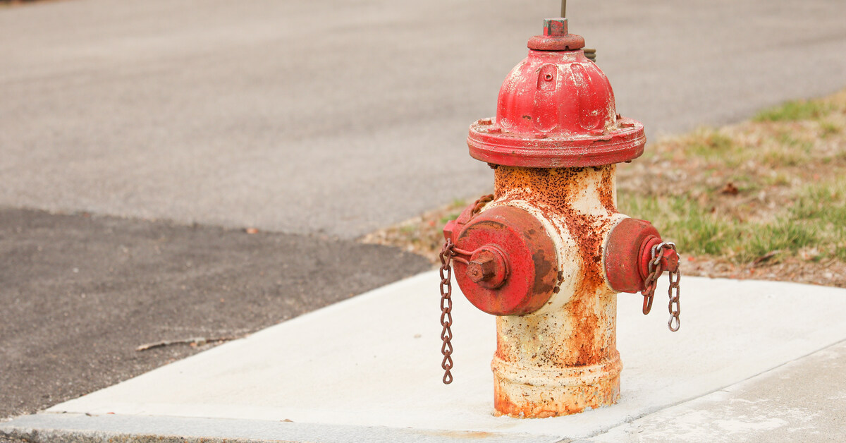 A white fire hydrant with a red bonnet and side outlets covered in rust-colored corrosion. The hydrant is on a fresh sidewalk.