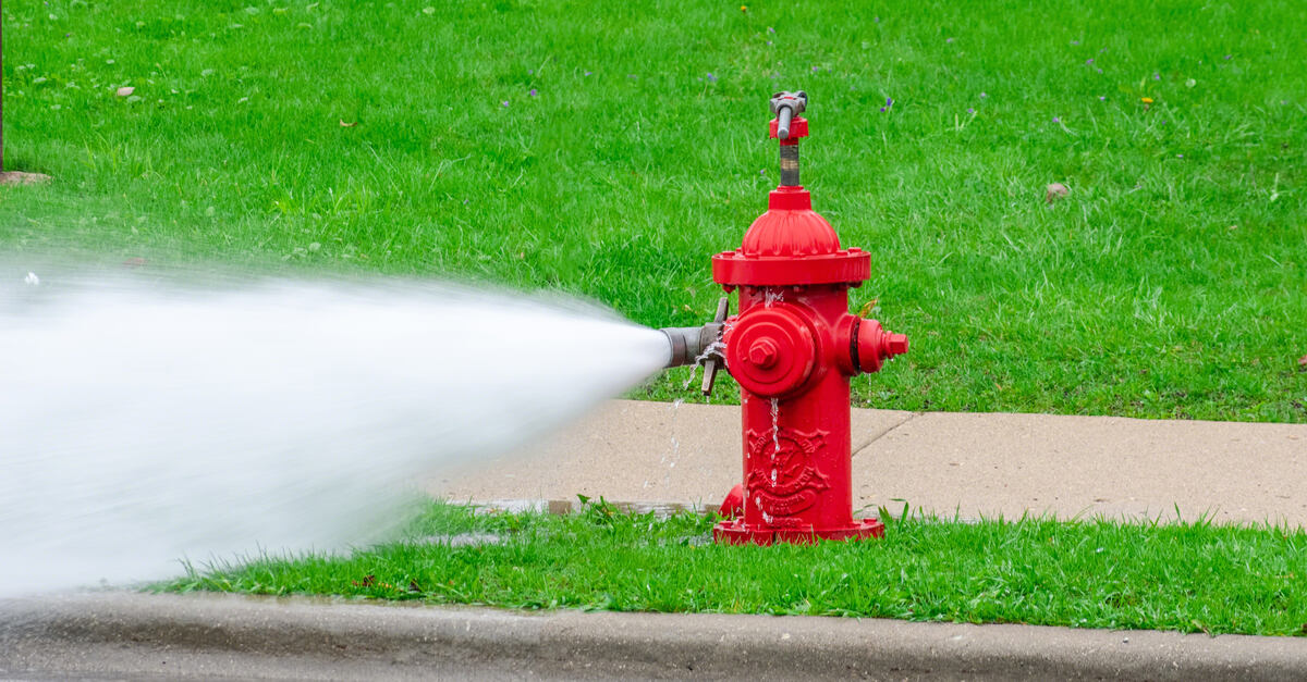 A hydrant wrench on top of a red fire hydrant keeping the valve open. Water is gushing out of the hydrant and into the street.