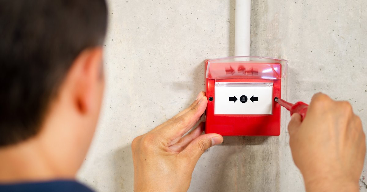 A man working on a fire alarm box. 