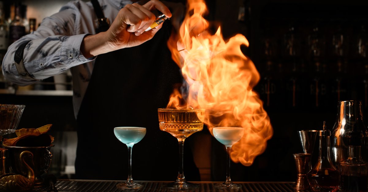 A bartender lighting some alcoholic beverage on fire. 