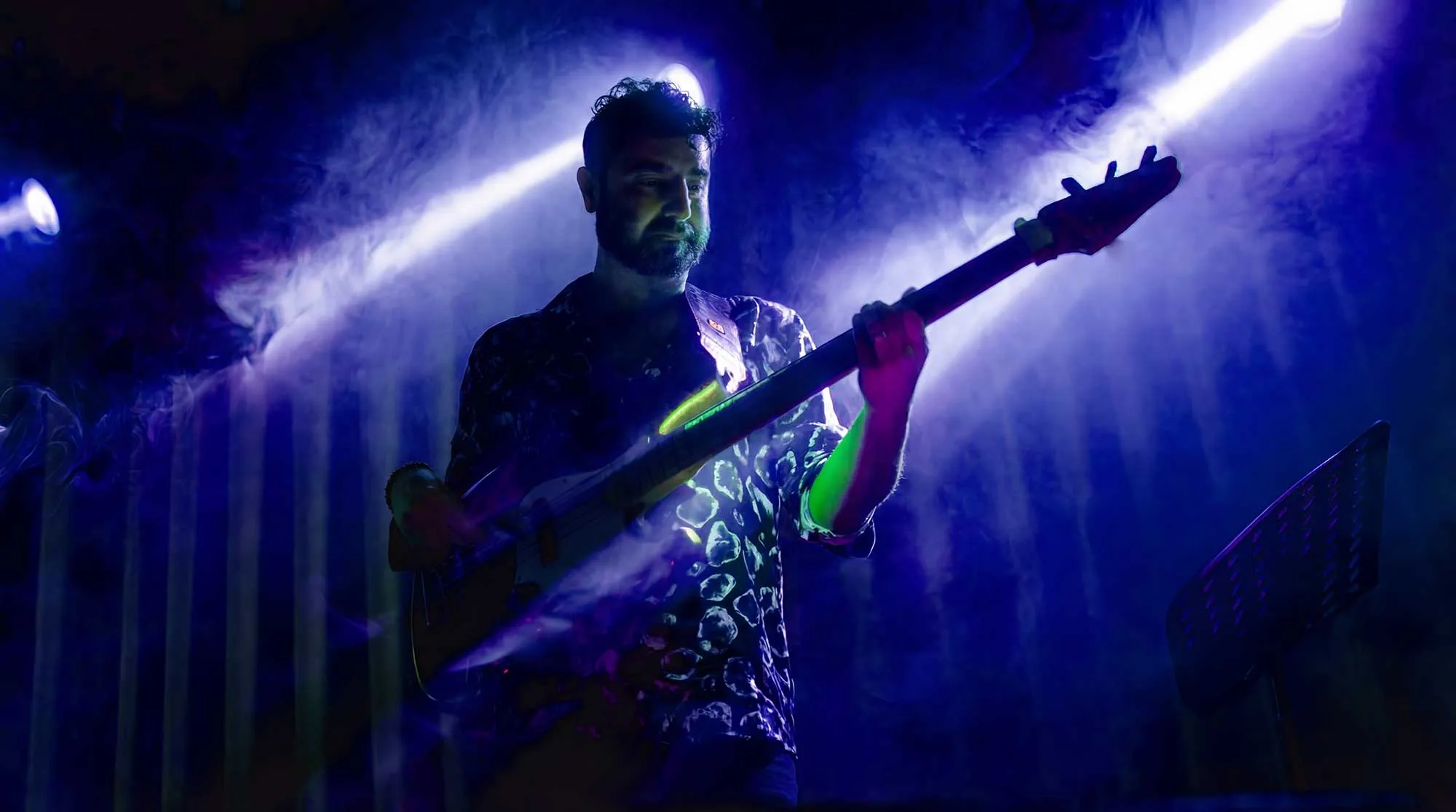 Man playing electric guitar on stage with blue lighting and smoke effects.