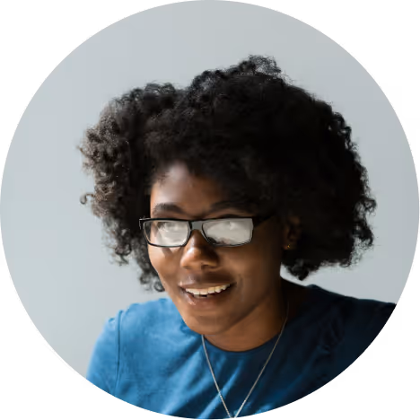 Smiling woman with curly hair wearing glasses and a blue shirt.