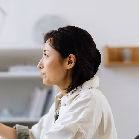 Profile of a woman with dark hair wearing a white jacket working indoors with blurred shelves in the background.