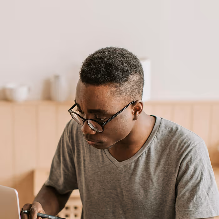 Man with glasses focused on writing or working at a laptop in a cozy indoor setting.