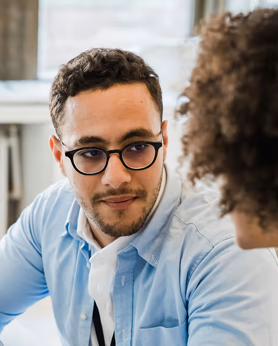 Man with glasses and beard wearing a blue shirt looking attentively at a person with curly hair.