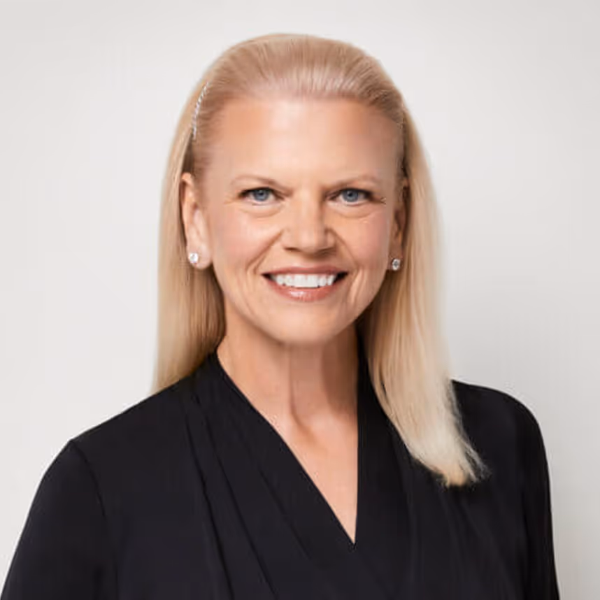 Smiling woman with straight blonde hair wearing a black top and pearl earrings against a plain background.