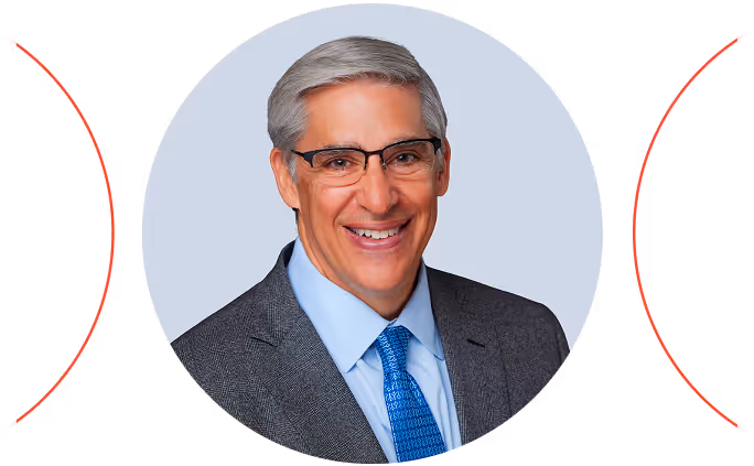 Smiling middle-aged man with gray hair wearing glasses, a gray suit, light blue shirt, and blue patterned tie.