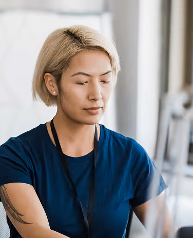 Woman with short blonde hair wearing a blue shirt and black lanyard looking down thoughtfully.