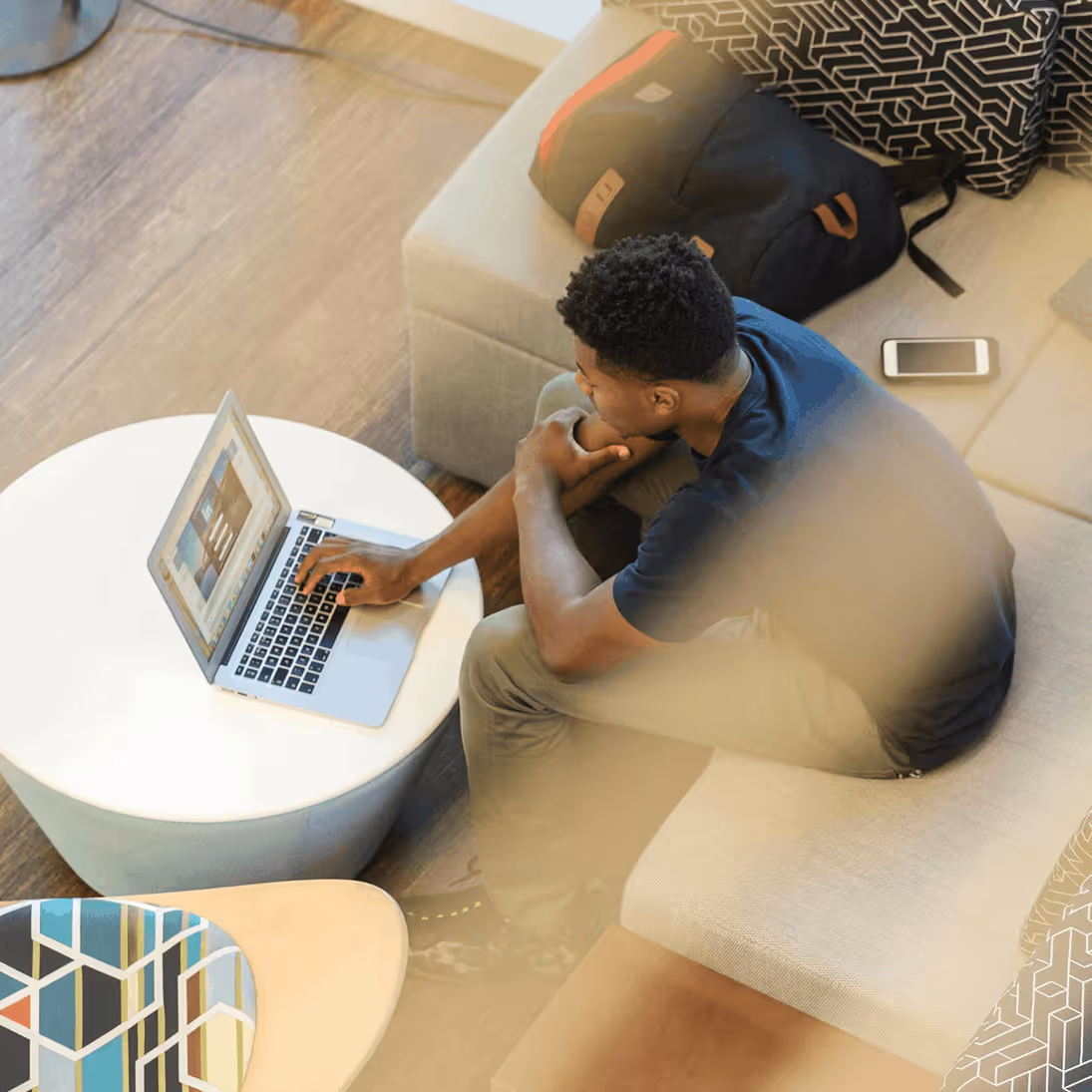 Man sitting on a couch using a laptop on a round table in a modern living room.
