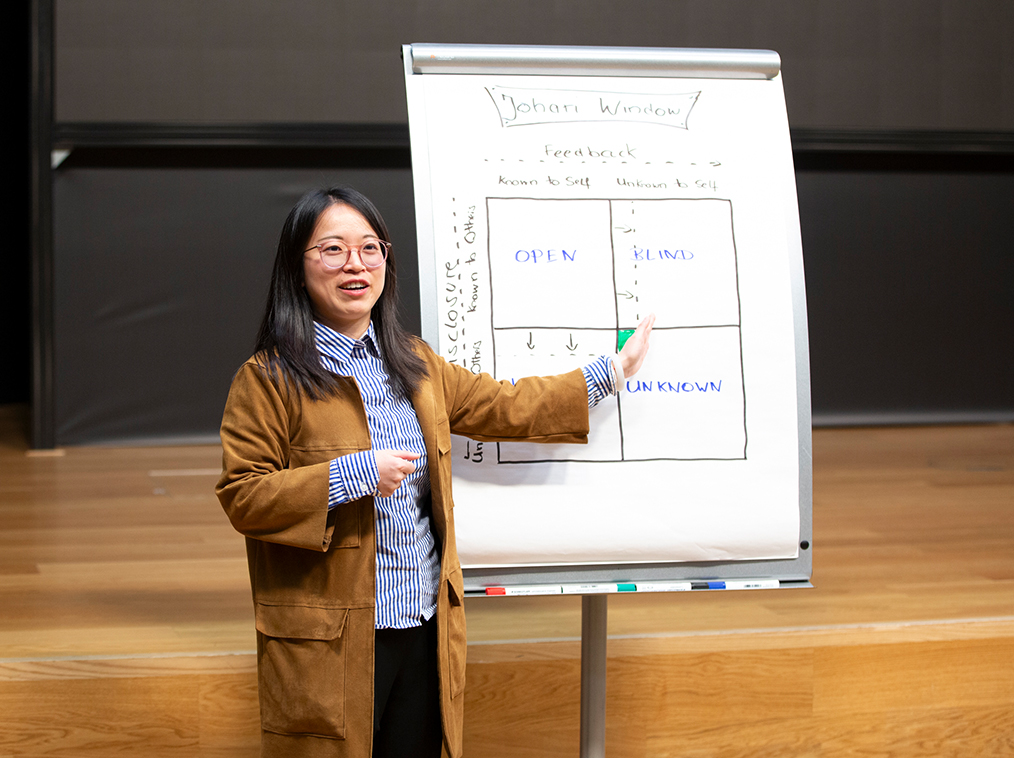 Woman with glasses presenting the Johari Window diagram on a flip chart during a workshop.