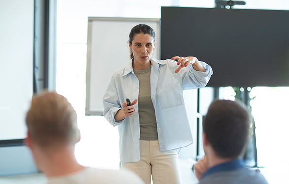 Woman giving a presentation to an audience in a bright conference room.