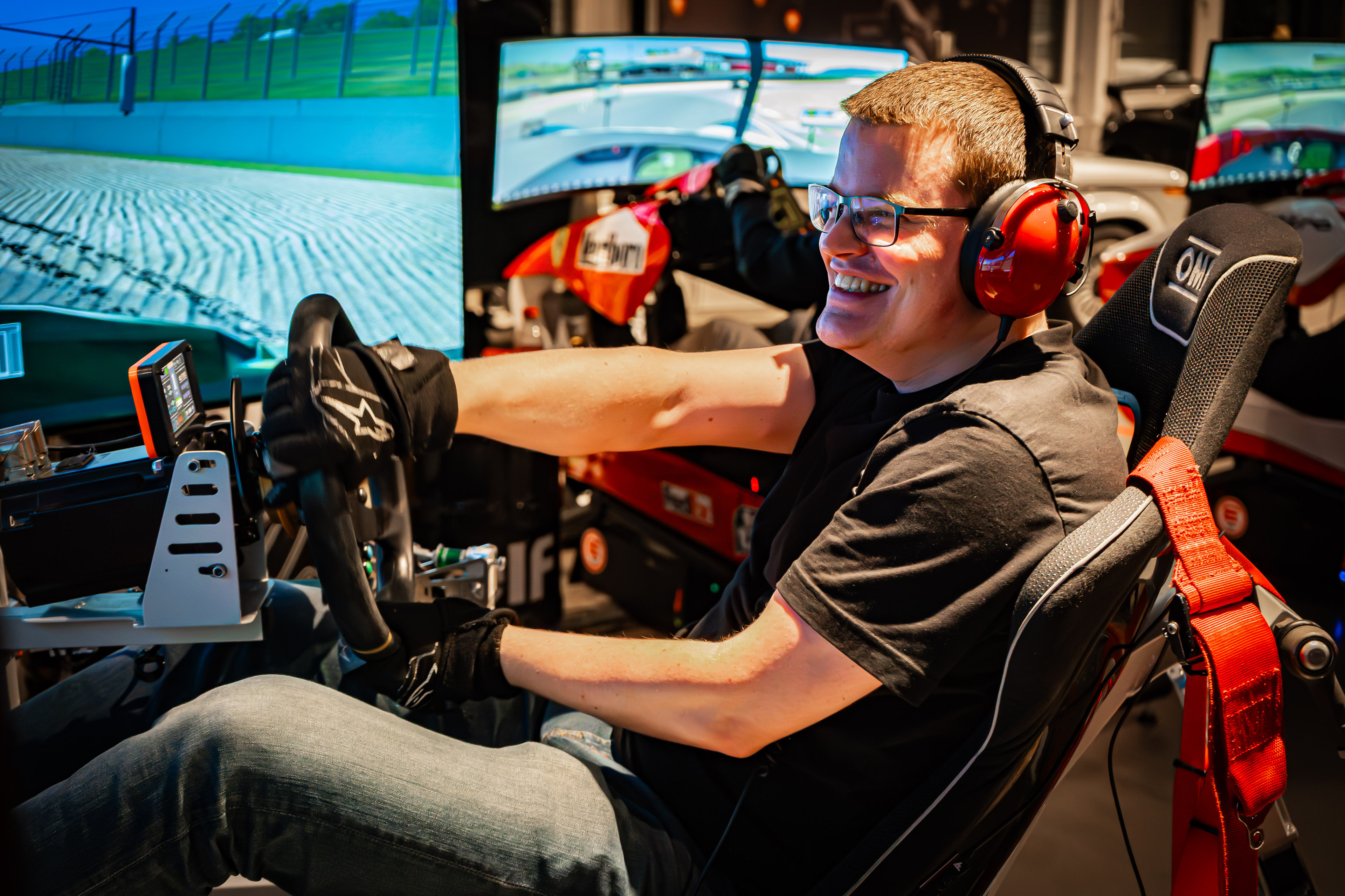 Mann sitzt in einer Rennautosimulation mit Lenkrad, Pedalen und gekrümmtem Bildschirm.