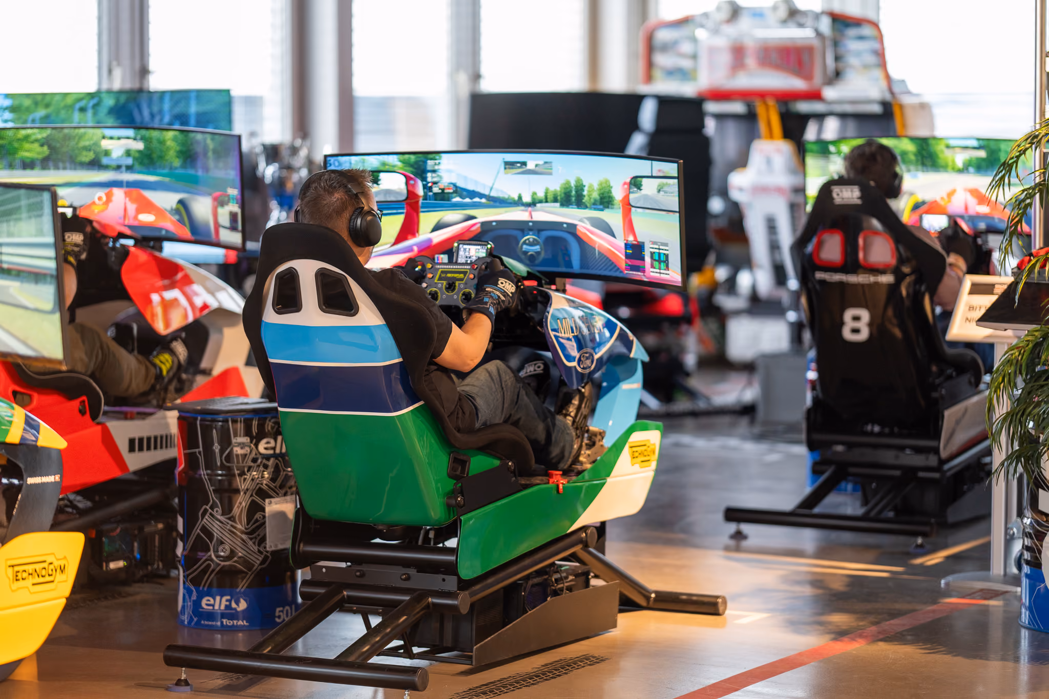Rennsimulator-Reihe mit Fahrer im Cockpit vor gebogenem Bildschirm in einer Motorsport-Location