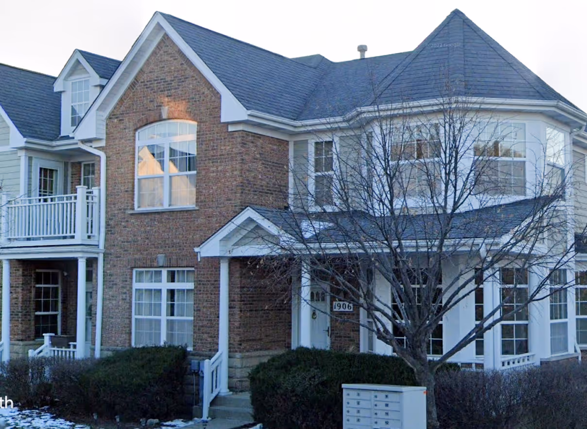 Two-story house with brick and siding exterior, multiple windows, a front porch, and a leafless tree in the front yard.