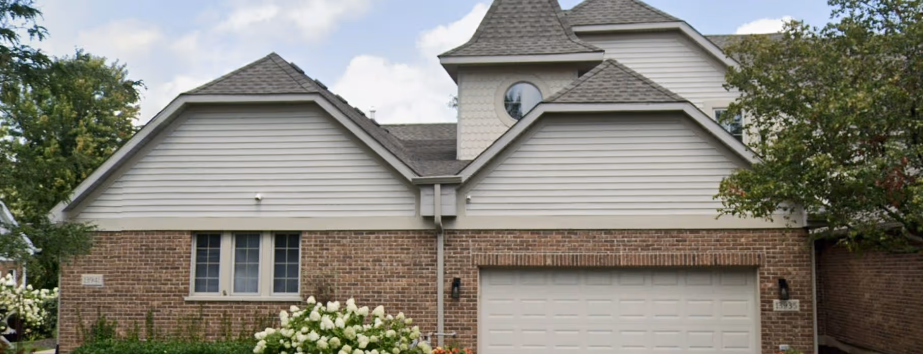 Modern two-story house with brick and light siding exterior, multiple gable roofs, a round window, and a white garage door.
