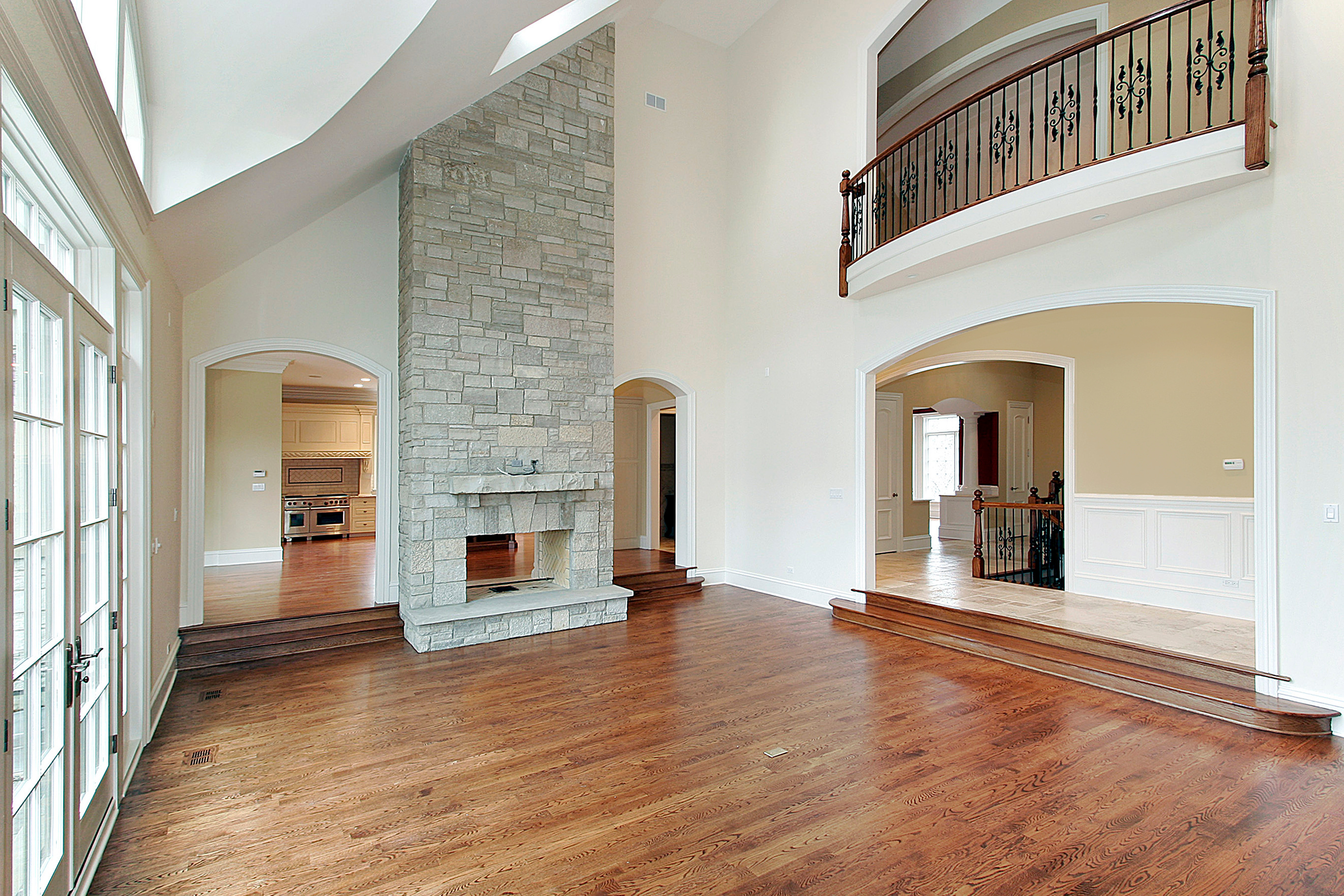 Glossy refinished hardwood in a big living room with a stone fireplace by Brazil Floors