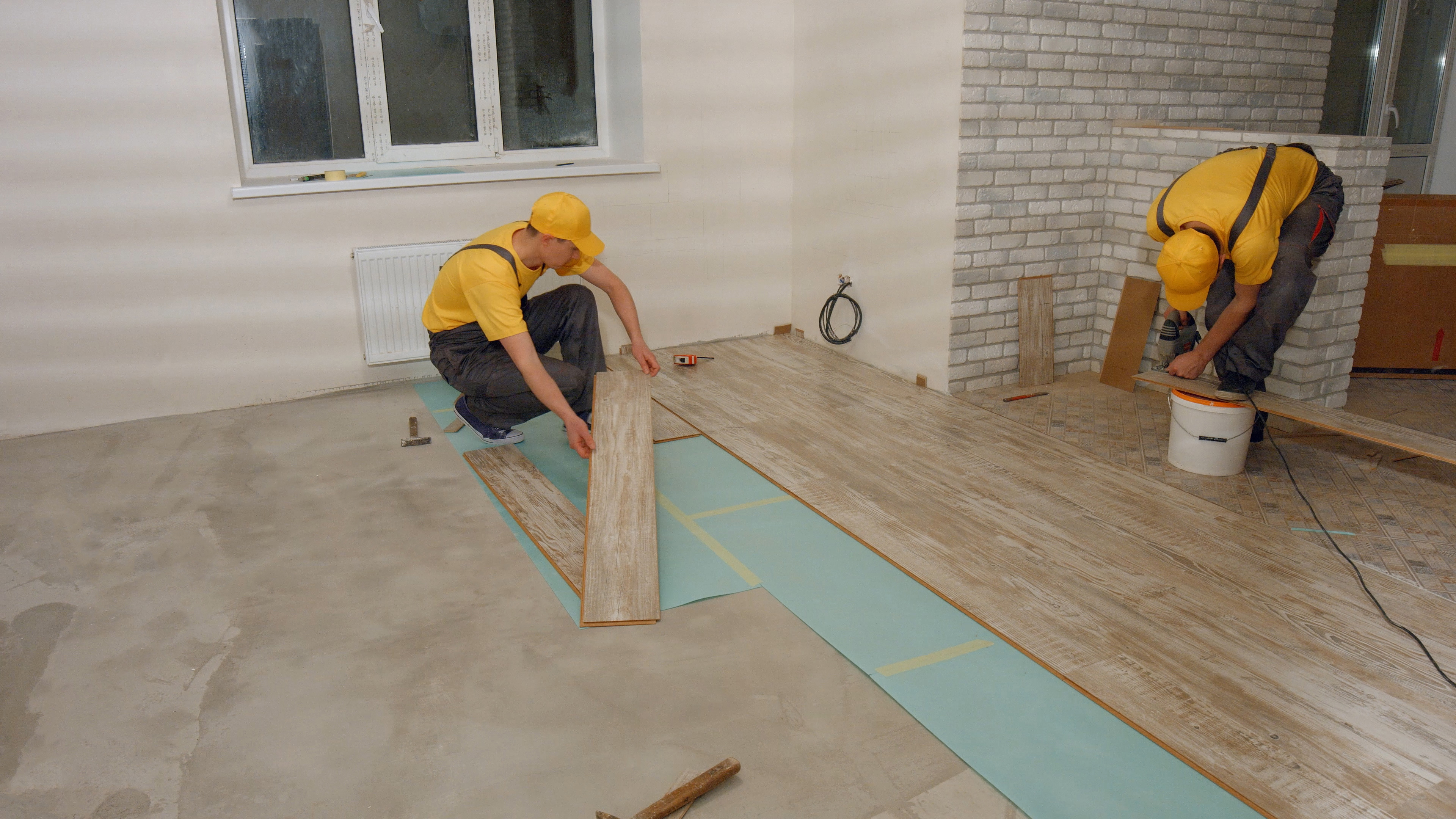 Two installers laying vinyl planks over a foam underlayment for Brazil Floors