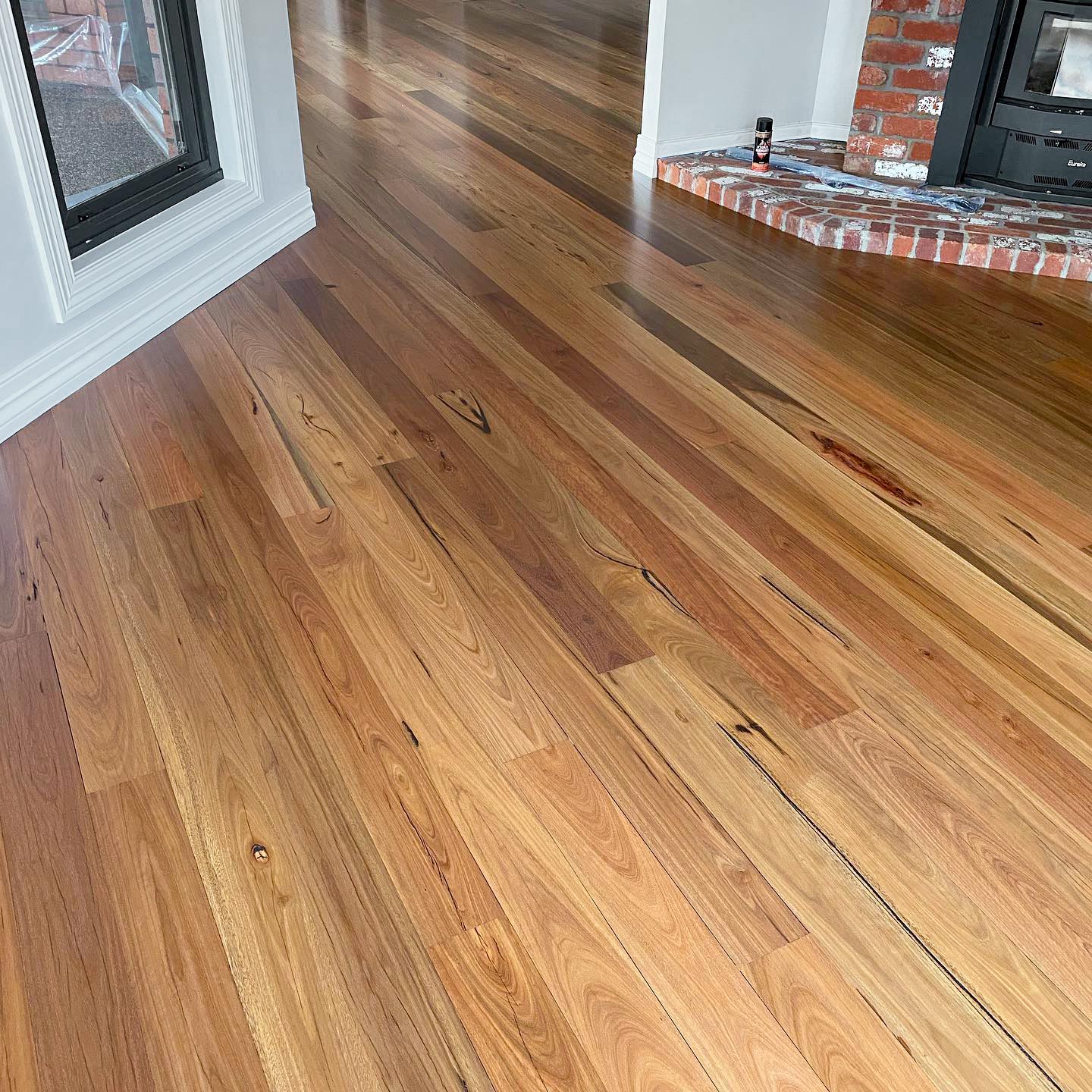 Repaired hardwood with a fresh finish beside a brick hearth by Brazil Floors