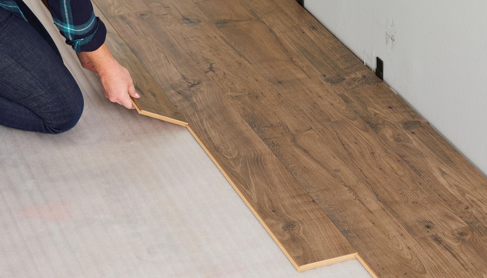 Installer pressing a new laminate plank into the row over gray foam underlayment, Brazil Floors