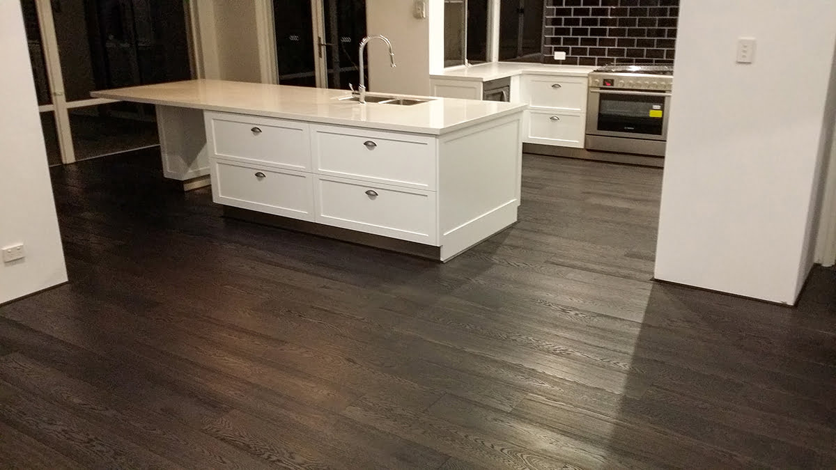 Dark stained hardwood floor in a kitchen with a white island, refinished in Glocester, RI