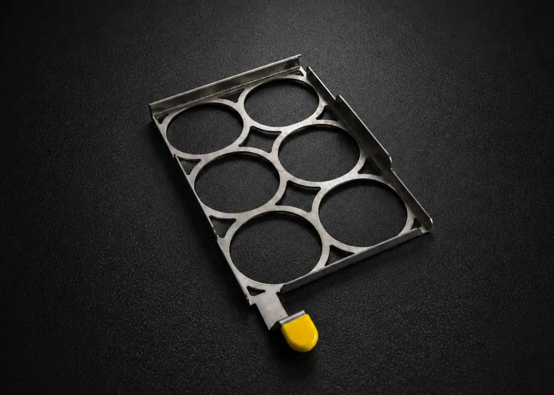 Precision-cut stainless steel component featuring a circular grid pattern and a yellow protective tip.