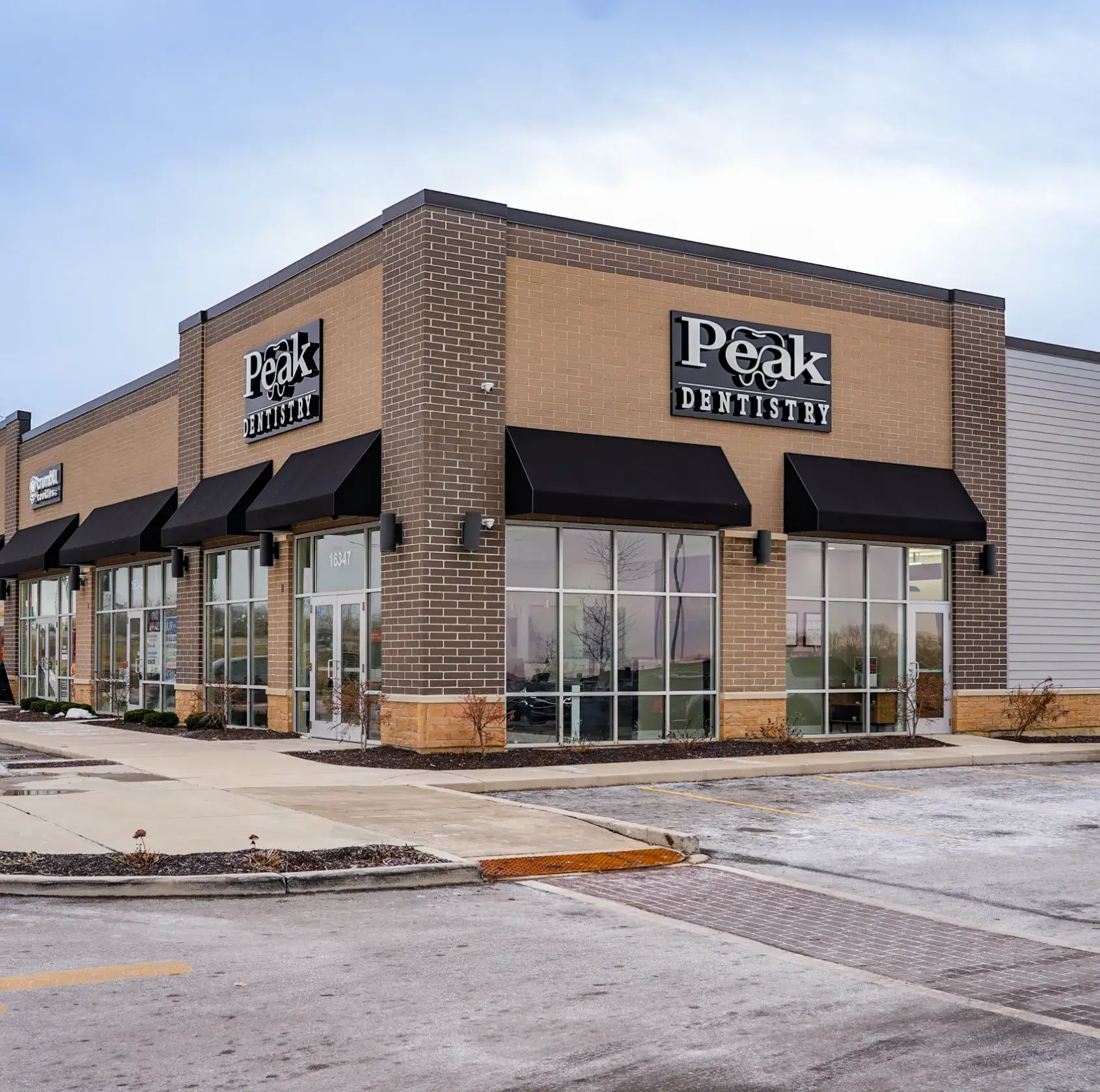 Corner view of a shopping plaza featuring Peak Dentistry with black awnings over large windows and entrance doors.