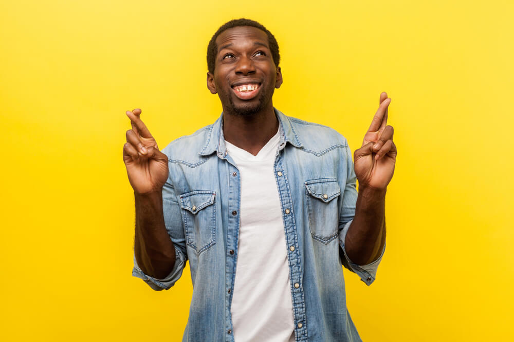 Portrait of a young man crossing his fingers hoping he wins social media contest.